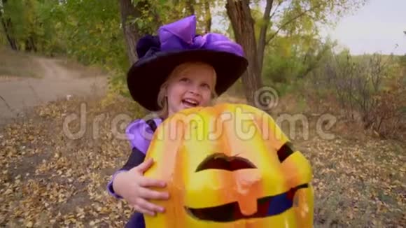 快乐的小美丽的女孩穿着女巫的服装和帽子抱着南瓜杰克秋天公园的万圣节视频的预览图
