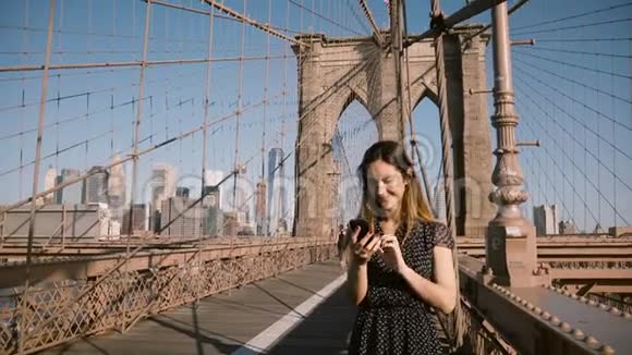 迷人的欧洲成年女性与朋友交谈使用智能手机视频呼叫应用程序布鲁克林大桥纽约市4K视频的预览图