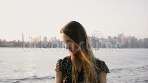 快乐的欧洲女孩的肖像留着飞扬的头发在日落海滩上微笑纽约的天际线4K视频的预览图