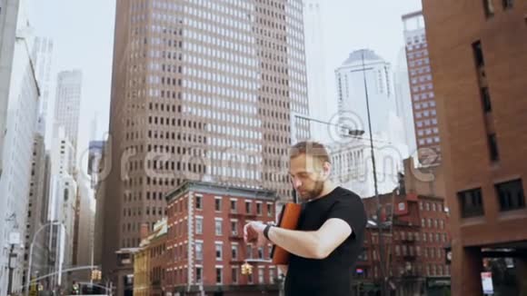 年轻英俊的商人拿着文件看着手表在纽约金融区散步慢动作视频的预览图