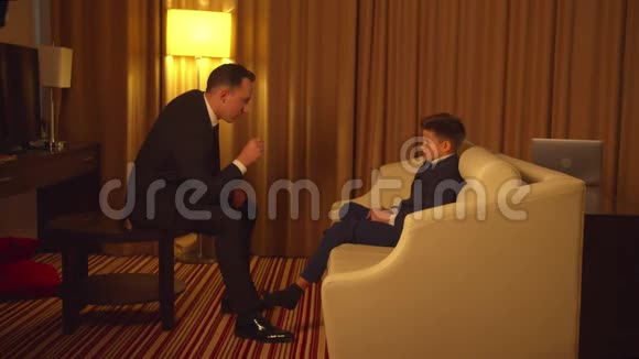 穿西装的商人坐在旅馆里和小男孩说话视频的预览图