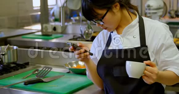 女厨师在喝咖啡时使用手机视频的预览图