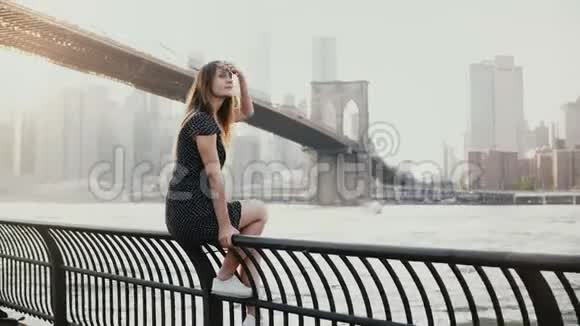 美丽的白种人年轻女子坐在纽约布鲁克林大桥的河堤围栏上杰斯基经过4K视频的预览图