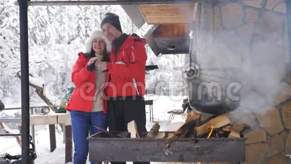 一对年轻快乐的夫妇在冬天的一天准备在一个木制森林房子的院子里明火视频的预览图