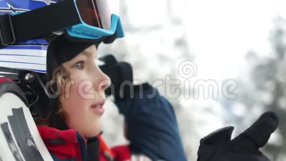 近距离拍摄戴着头盔和护目镜的少年男孩站在滑雪缆车舱里孩子开心地笑了有趣的假期视频的预览图