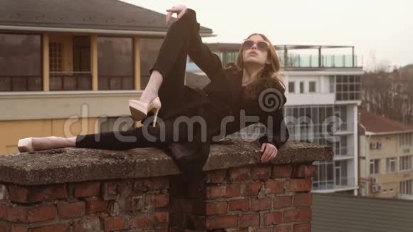 时尚模特摆姿势戴着太阳镜坐在墙上的漂亮年轻女子视频的预览图