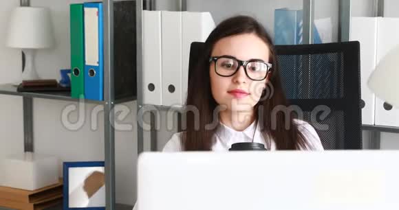 女商人在现代办公室里喝咖啡在笔记本电脑前微笑视频的预览图