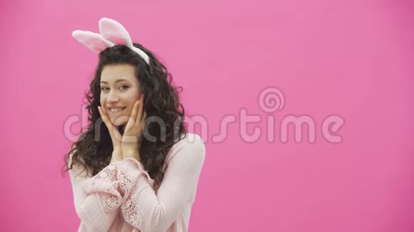 复活节的节日复活节兔子耳朵上带着微笑的年轻女子在粉色背景上跳来跳去看着复制品视频的预览图