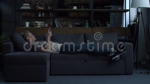 休闲少年躺在沙发上用数码平板电脑视频的预览图