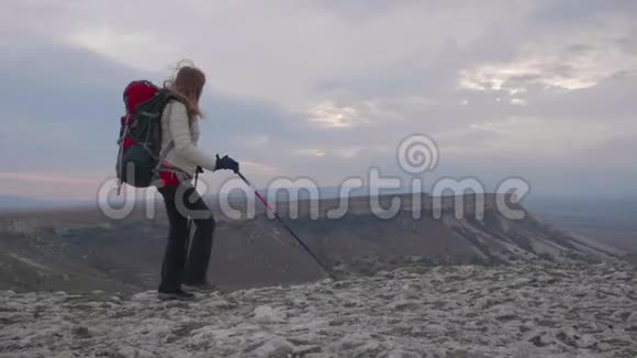年轻的徒步旅行者女人带着背包和登山杆沿着岩石的边缘行走视频的预览图