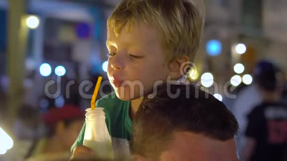 在泰国的一个夜市上小男孩坐在父亲的脖子上着新鲜的果汁泰国菜的概念亚洲视频的预览图