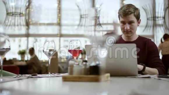 一个年轻的商人坐在一家咖啡馆的桌子旁用iphone一边笑一边看着过路人视频的预览图