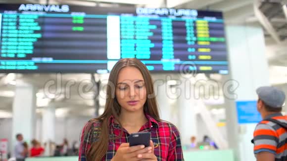 年轻微笑的女士使用智能手机在到达台背景上检查航班的照片视频的预览图
