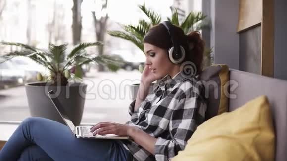 漂亮开朗的女人在时髦的房间里用笔记本电脑听音乐耳机坐在休闲沙发上视频的预览图