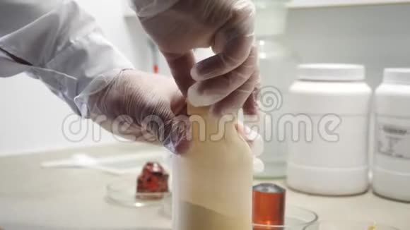 戴着白色防护手套的人的手的特写镜头打开一个瓶子上面有白色的化学粉末视频的预览图
