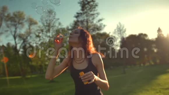 美丽的红发年轻女子的肖像在公园里吹泡泡视频的预览图