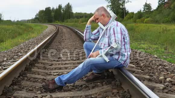 一个拄着拐杖坐在铁路上哭泣的沮丧的男人视频的预览图