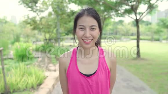 健康美丽的年轻亚洲跑步女子在城市公园的街道上跑步后感到快乐的微笑和寻找相机视频的预览图