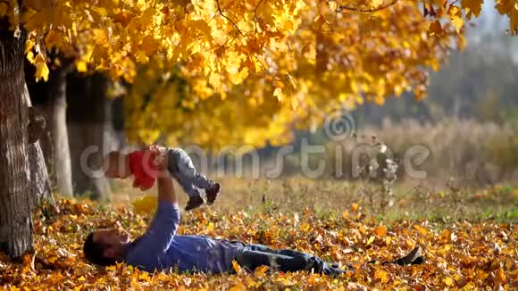 年轻的父亲躺在秋叶上把孩子抱上了天堂视频的预览图
