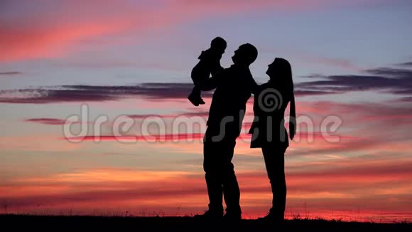 父母和婴儿剪影和夕阳红的天空父亲养育孩子嬉戏视频的预览图