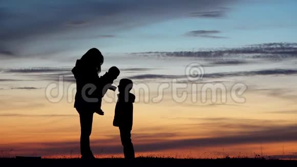 妈妈带着两个孩子剪影宝宝和哥哥一起玩日落的天空视频的预览图