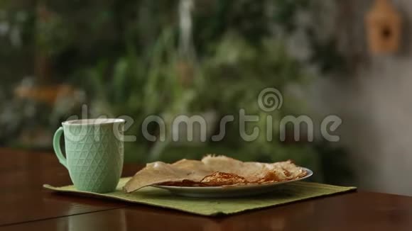 桌子上有蒸汽的杯子和煎饼背景中的绿色植物厨房美丽的家视频的预览图
