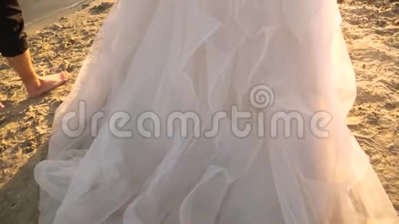 新郎赤着脚新娘穿着白色连衣裙沿着河沿海滩散步情侣在沙滩上散步视频的预览图