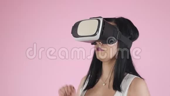 美丽的女人触摸空气在VR体验期间隔离在粉红色女孩使用虚拟现实耳机视频的预览图