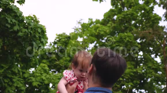 爸爸在公园夏天和孩子玩小女孩在爸爸的手里跳着笑着慢动作视频的预览图