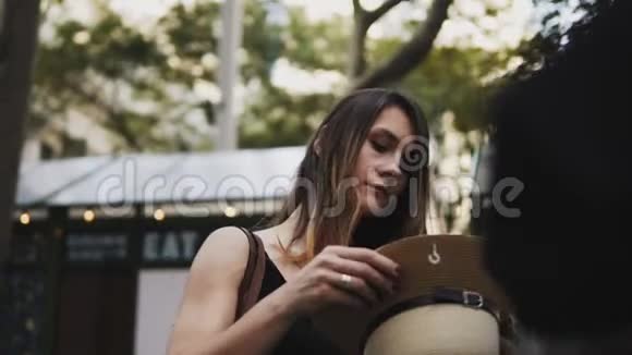 街头集市上的年轻快乐女人美丽的女人站在外面试着戴上帽子微笑着视频的预览图