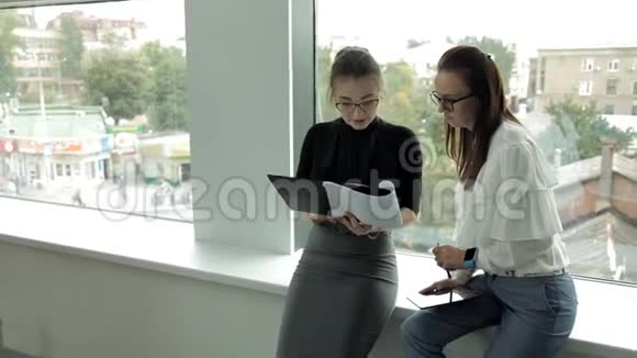 两个戴着眼镜的年轻商务女孩在商务中心工作站在窗口讨论工作视频的预览图