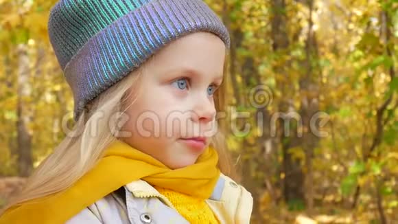 秋天戴着蓝色霓虹灯色帽子和黄色围巾的小可爱女孩在公园里微笑视频的预览图