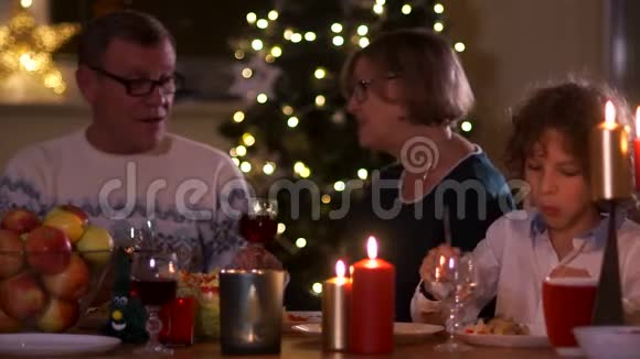 烛光下圣诞餐桌上可爱的一家人祖母和祖父喝着杯子里的酒卷曲的孙子视频的预览图