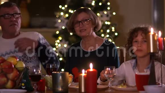 有家人的幸福老年妇女在圣诞餐桌上举起一杯圣诞装饰品桌子上的蜡烛视频的预览图