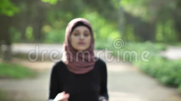 一个年轻女孩在头巾的框架内奔跑的肖像关于自然在一个公园的背景50英尺视频的预览图