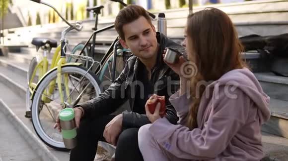 可爱的情侣坐在楼梯上吃牛角面包在户外喝咖啡坐在格子呢上视频的预览图