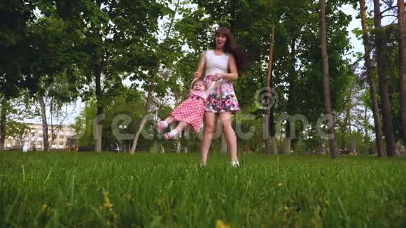 妈妈和一个快乐的笑女儿在空中盘旋家长在夏日公园的草地上玩耍视频的预览图