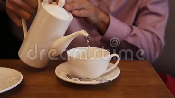 男人用一个白茶壶把热水倒入木桌上的白杯里泡茶视频的预览图