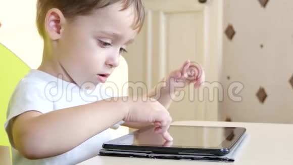 快乐的孩子坐在桌子旁摸着触摸屏平板一个孩子在玩平板电脑正在微笑视频的预览图