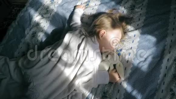 可爱的小女孩金发睡在床上被阳光照亮带着一只泰迪兔子视频的预览图