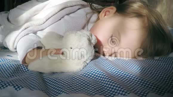 可爱的小女孩金发睡在床上被阳光照亮带着一只泰迪兔子视频的预览图