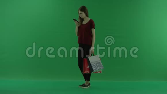 漂亮的购物女人用手机拿着购物袋女士正在上网或打字视频的预览图