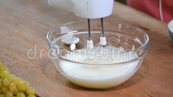女性的手在碗里加入一个糖在蓝色的木桌上用搅拌器搅拌蛋清一步一步的食谱视频的预览图