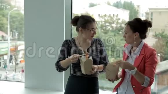 两个年轻的商业女孩在银行工作在窗口吃午餐吃中国面条讨论生意视频的预览图