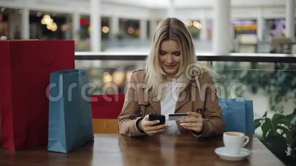 女孩子在咖啡馆里拿着购物袋坐着一张信用卡视频的预览图
