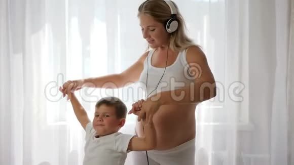 年轻的妈妈抱着儿子她的手听音乐戴着耳机跳舞视频的预览图