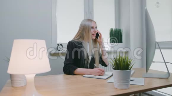 商务女性在办公室谈论智能手机优雅的年轻金发女性穿着办公室西装坐在工作场所和视频的预览图
