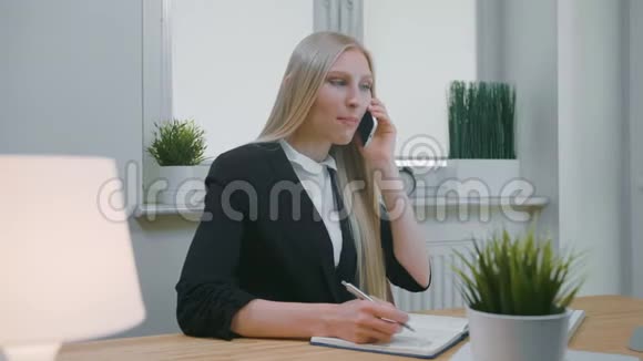 商务女性在办公室谈论智能手机优雅的年轻金发女性穿着办公室西装坐在工作场所和视频的预览图