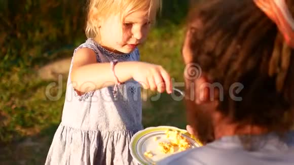 一个小女孩用勺子喂她爸爸在村子里的夏日夜晚视频的预览图