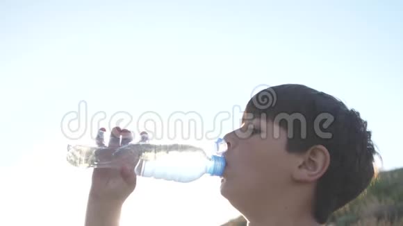 男孩在晴朗的天空中从塑料瓶里喝水视频的预览图